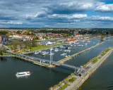 Widok na port w Giżycku, gdzie cumują liczne jachty i statki. Nowoczesny most pieszy łączy brzegi, a w tle rozciąga się miasto. To idealne miejsce na odkrywanie giżycko atrakcje.