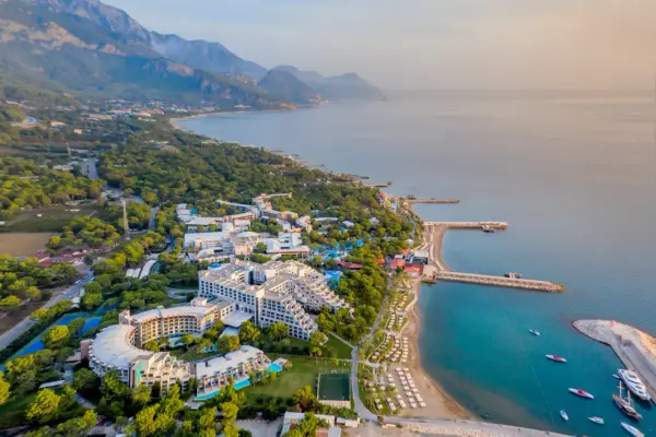 Widok z lotu ptaka na Rixos Sungate, luksusowy kurort nad turkusowym morzem, otoczony zielenią i górami.