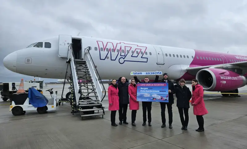 Grupa osób pozuje przed samolotem Wizz Air, trzymając tablicę z informacją o nowych trasach, w tym lotach Szczecin-Bergen.